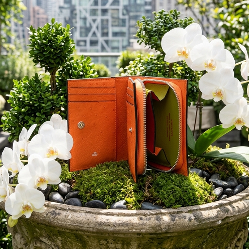 Orange wallet on a bed of moss with white flowers and greenery in the background