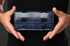 Blue textured wallet held by a person against a dark background