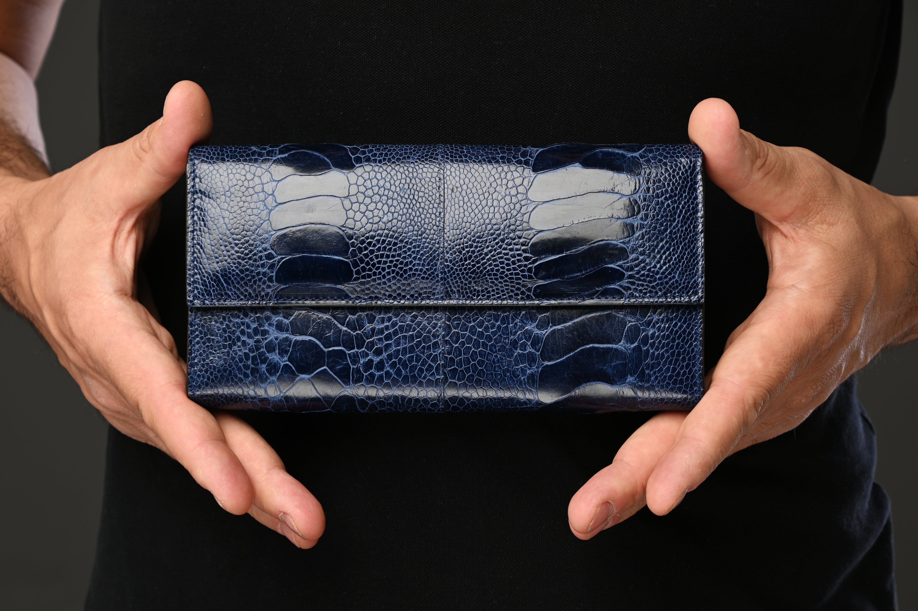 Blue textured wallet held by a person against a dark background