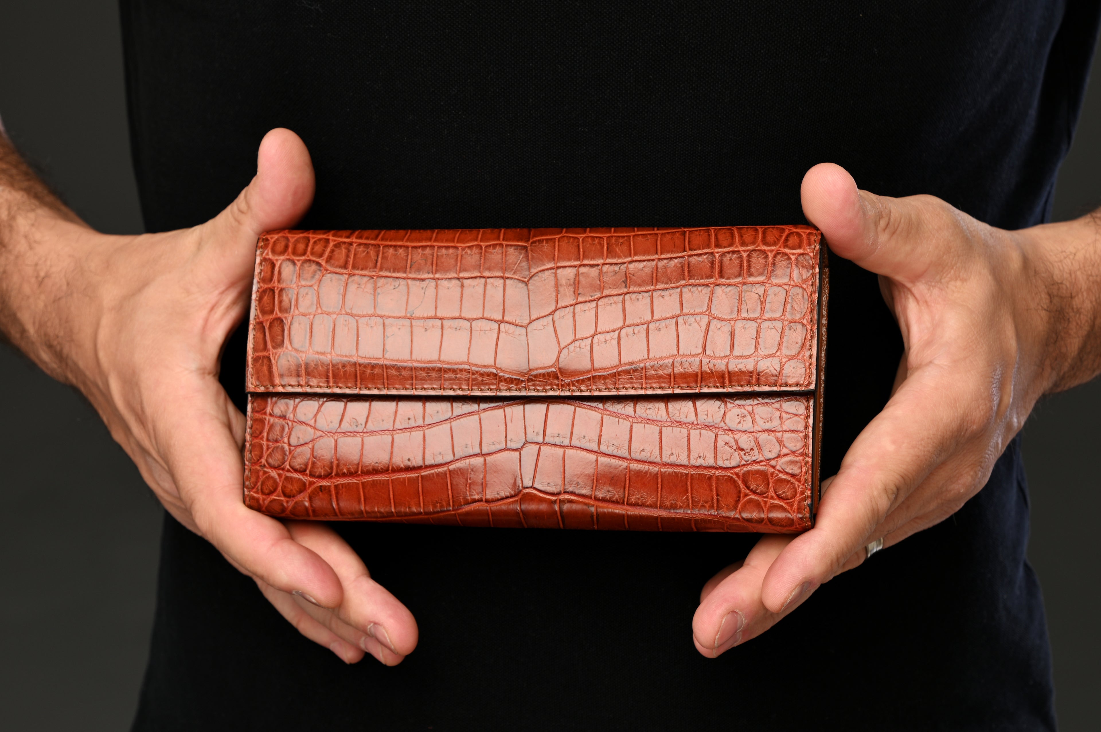 Brown crocodile skin wallet held by a person against a black background